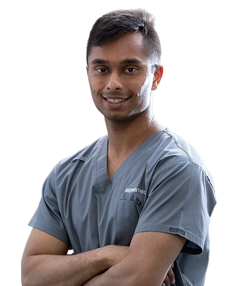Photo shows a young male Aspen Medical clinician in grey scrubs, smiling with his arms crossed.