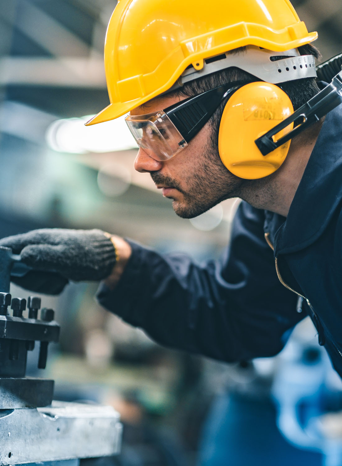 Photo shows an energy sector worker wearing a yellow hardhat, ear covers, eye protection and gloves to operate machinery.